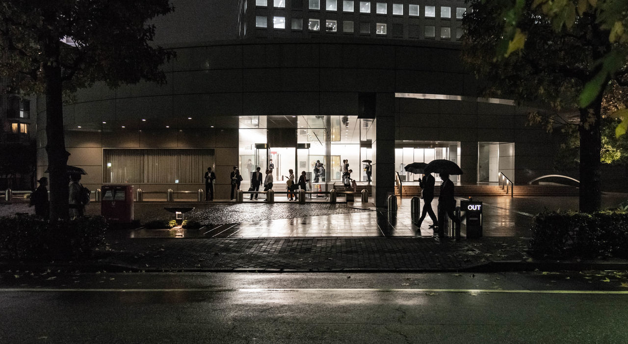 PEOPLE ON ILLUMINATED STREET AMIDST BUILDINGS AT NIGHT