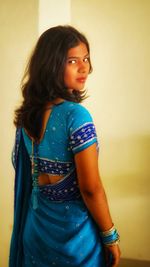 Portrait of smiling young woman standing against wall