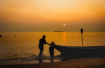 Silhouette people on beach against sky during sunset