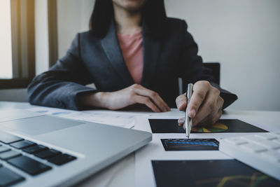 Midsection of businesswoman holding pen pointing at document