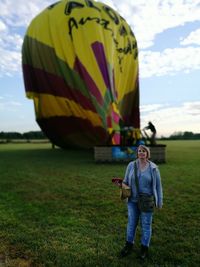 Full length portrait of smiling woman standing on field against sky