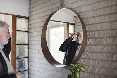 Senior man looking at mirror while standing in room