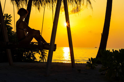 Silhouette man sitting on beach against sky during sunset