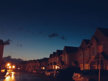 City street by buildings against sky at night