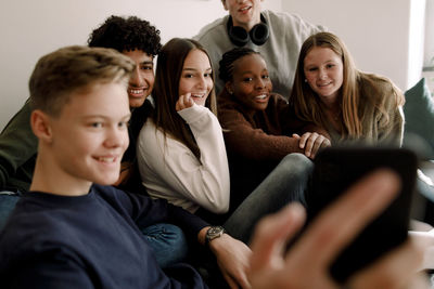 Smiling teenage boy taking selfie with male and female friends at home