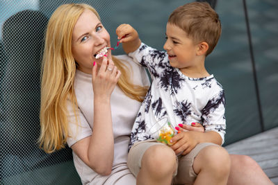 Happy blond woman and little boy sitting on terrace and eating sweets. mother and son enjoy