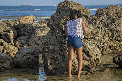 Rear view of woman standing on rock by sea