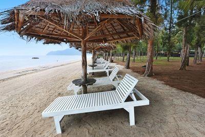 Empty chairs and tables at beach against sky