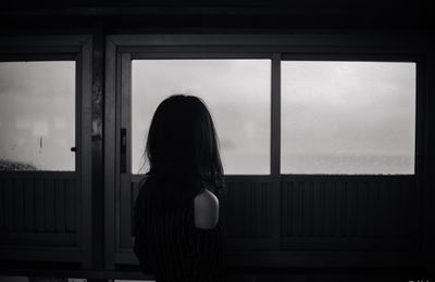 Rear view of woman looking towards wet window at home