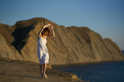 Woman standing on rock by sea against sky