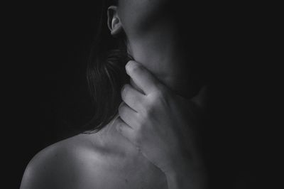 Midsection of topless woman choking throat against black background