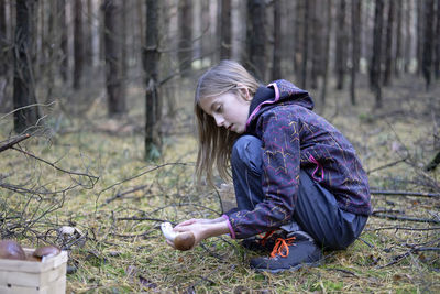 Side view of cute girl collecting edible mushroom in forest