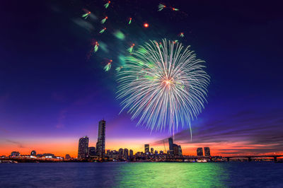 Low angle view of firework display over river in city