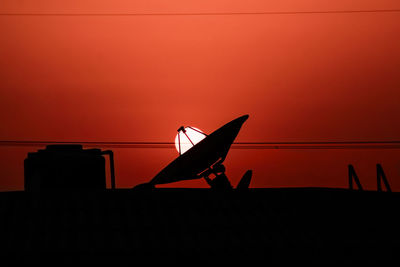 Silhouette satellite dish on building terrace against orange sky