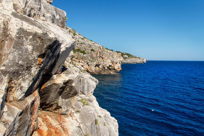 Rock formation by sea against clear blue sky