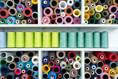 Set of colorful spools of threads for sewing stacked together on white shelves at wall in professional modern light atelier