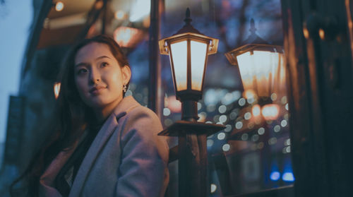 Portrait of smiling young woman standing against illuminated lamp