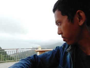 Close-up portrait of boy looking at railing against sky