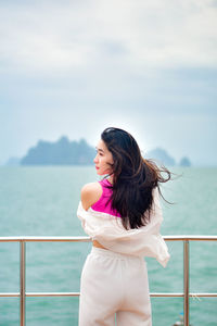 Young woman looking away while standing against sea