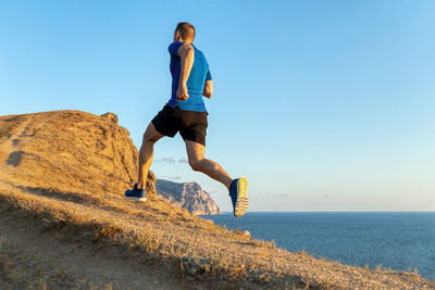 Back man runner run uphill in background sky and sea