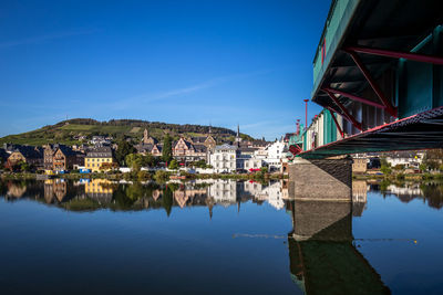 Bridge over river by buildings against blue sky