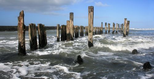 Wooden posts on beach against sky