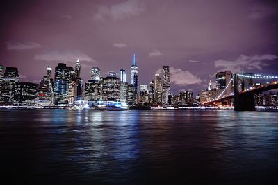 Illuminated city by river against sky at night