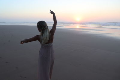 Woman standing at beach against sky during sunset