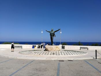 Statue on footpath by sea against clear blue sky