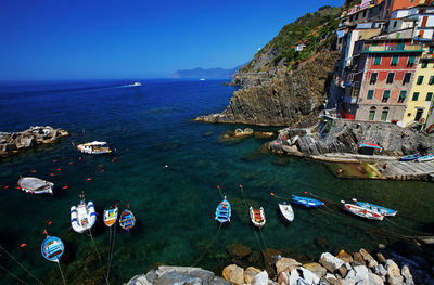 High angle view of boats moored on sea by residential buildings against clear blue sky