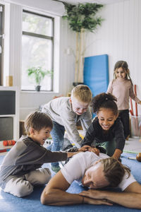 Cheerful multiracial children playing with male teacher in day care center