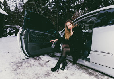 Full length portrait of young woman sitting in car during winter