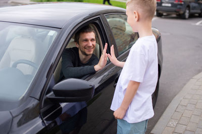 A cute child accompanies a happy father to work. dad is sitting in the car. give five