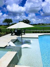 Lounge chairs by swimming pool against sky