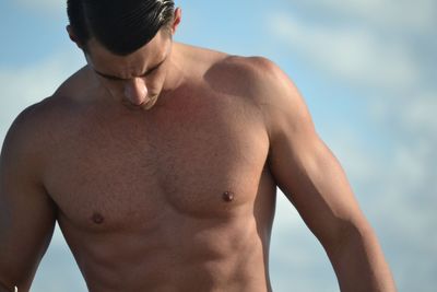 Shirtless man looking down while standing against sky