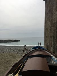 Boats moored by wall on seashore against sky