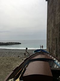 Boats moored by wall on seashore against sky