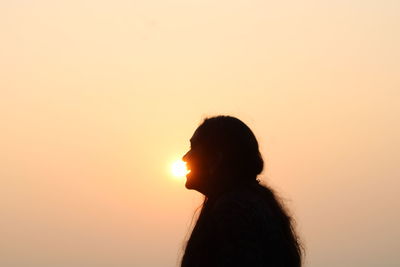 Side view of young woman against orange sky a day with a beautiful sunrise. 