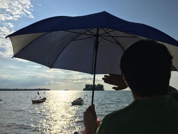 Rear view of man with umbrella standing by sea against sky