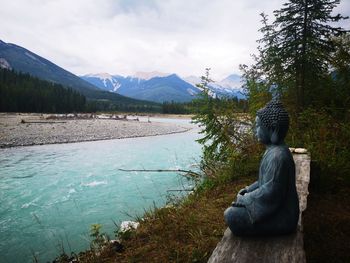 Rear view of woman sitting by lake against sky