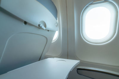 Plane window with white sunlight. empty plastic airplane tray table at seat back. economy class.