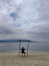 Rear view of woman swinging on beach against sky