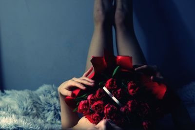 High angle view of woman holding rose bouquet while lying on bed at home