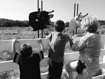 Rear view of siblings standing on field against sky