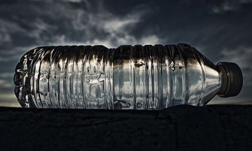 Close-up of water bottle on floor against cloudy sky