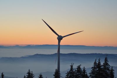 Windmill against fog covered silhouette mountains at sunset
