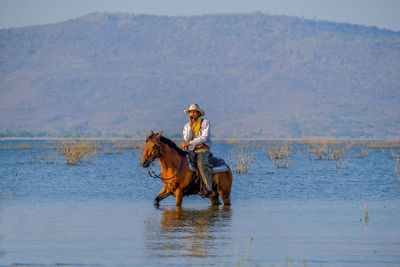 Mature man riding horse in lake against mountain