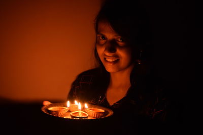 Portrait of smiling young woman holding illuminated diya 