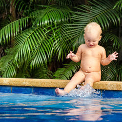 Naked girl playing with water while sitting at poolside