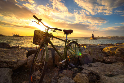 Bicycle on beach against sky during sunset